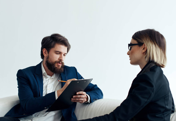 Business man with documents explains something to a young woman Sitting on a sofa indoors - 写真・画像