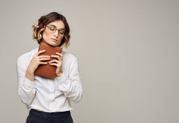 Pretty woman in glasses and a white shirt on a gray background with a book in her hands - 写真・画像