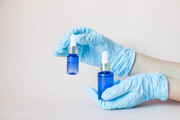 Bottles with serum for the face in his hands in protective medical rubber gloves on a light background. Beauty industry. - Photo, Image