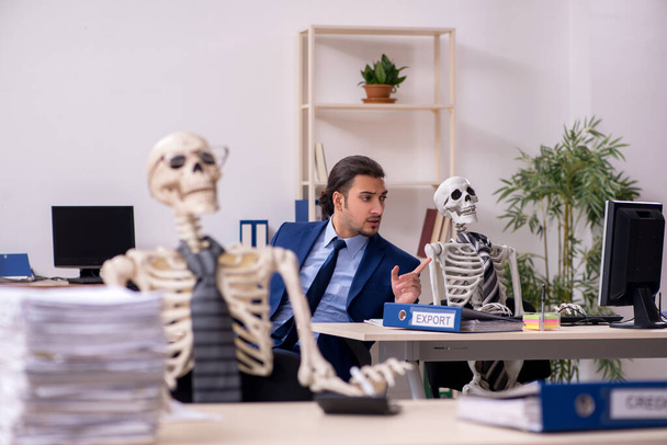 Jovem funcionário do sexo masculino com esqueletos no escritório - Foto, Imagem