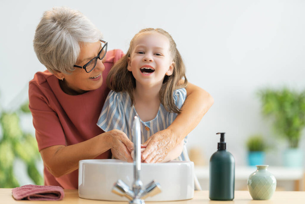 A cute little girl and her grandmother are washing their hands. Protection against infections and viruses.   - Fotoğraf, Görsel