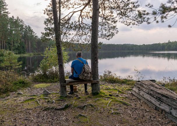 silueta de un hombre sentado en un banco junto al lago pantano, paisaje del lago pantano, tiempo de otoño - Foto, Imagen