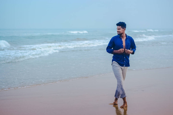 Σέξι ινδική άνδρες μοντέλο περπάτημα στην παραλία θέα στη θάλασσα φόντο με χώρο για αντίγραφο κειμένου. Όμορφοι και με αυτοπεποίθηση άνδρες. Εξωτερική πορτρέτο του περπατήματος νεαρός Ασιάτης Ινδός στην παραλία. - Φωτογραφία, εικόνα