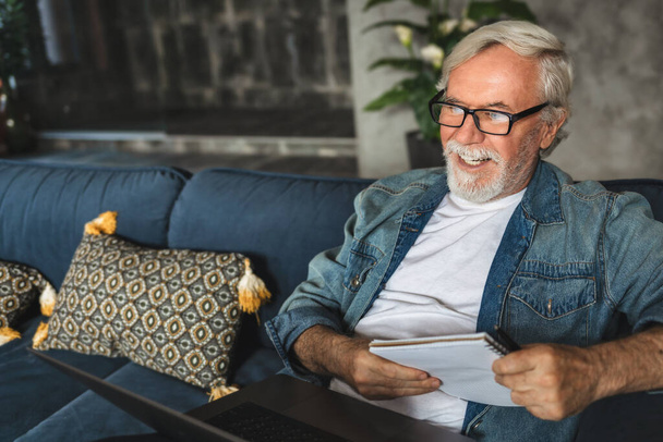 Smiling elderly professor conduct online lesson using laptop computer, Senior man speak talk on video call while Sitting on sofa - Foto, afbeelding