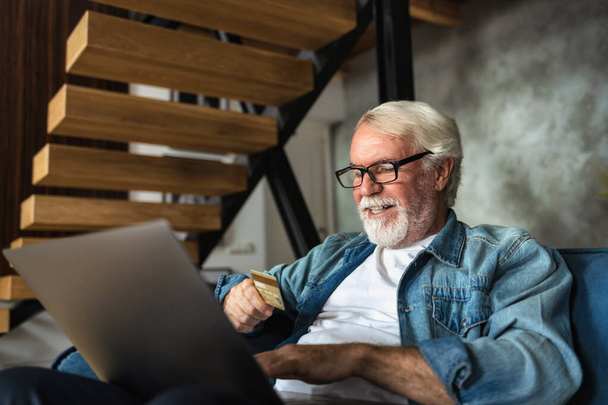 Portrait of man of retirement age shopping online on laptop pay with credit card. Senior person place an order for a purchase of goods online - Foto, afbeelding