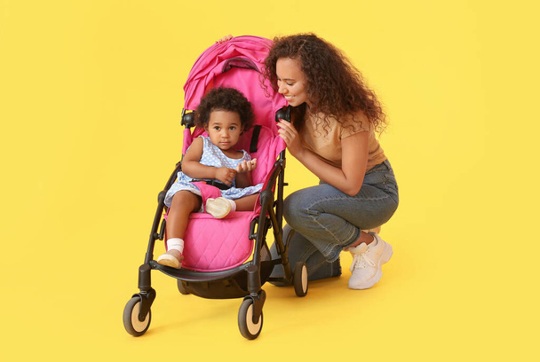 Afroamerikanerin und ihr süßes Baby im Kinderwagen auf farbigem Hintergrund - Foto, Bild