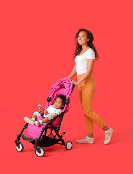 Mujer afroamericana y su lindo bebé en cochecito sobre fondo de color - Foto, imagen