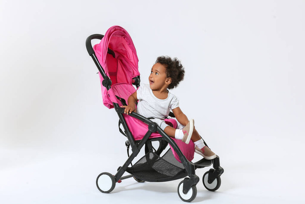 Leuke Afro-Amerikaanse baby in kinderwagen op lichte achtergrond - Foto, afbeelding