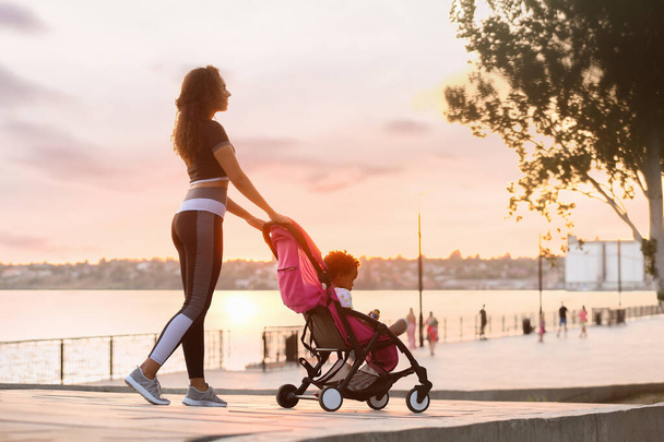 Sporty African-American woman and her cute baby in stroller outdoors - Photo, Image