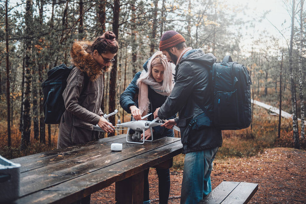 Group of three students tuning quadcopter at table in forest - Photo, image