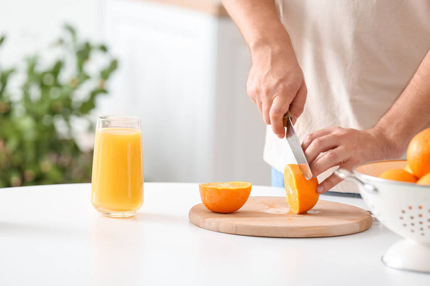 Man snijdt oranje in keuken, close-up - Foto, afbeelding