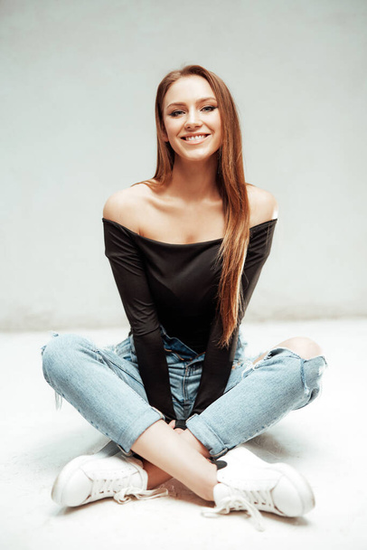 Smiley girl sits on floor in white background looking at camera - Photo, Image