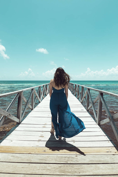 A vertical shot of a gorgeous female walking on a pier in the background of a calm sea - Photo, Image