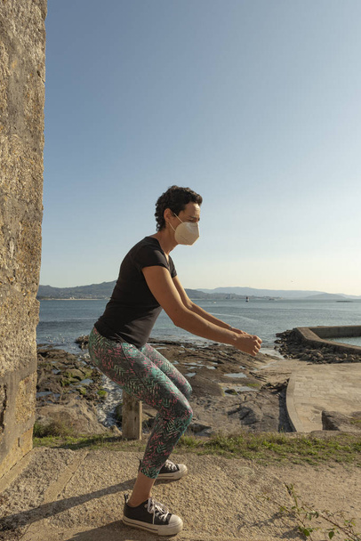 A young female in a medical mask during morning workout near the sea - the concept of new normal - Foto, Imagen