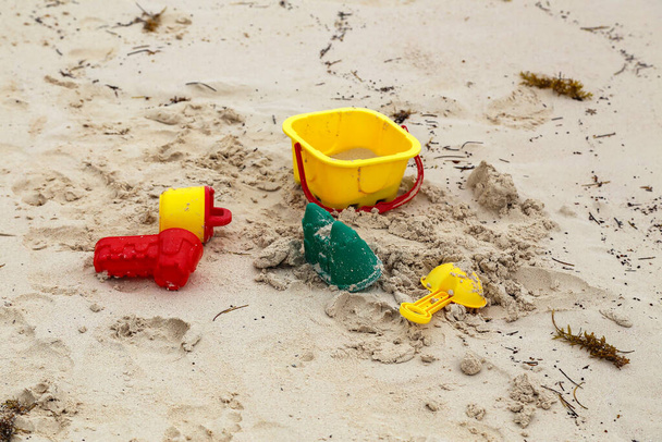 A high angle shot of bright baby toys in the sand on the beach - Fotó, kép
