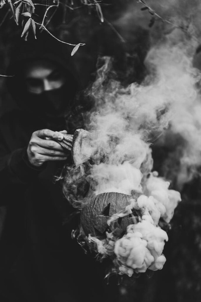 A vertical grayscale shot of a man holding a carved pumpkin with smoke - the concept of Halloween - Fotoğraf, Görsel
