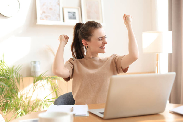 Happy entrepreneur woman sit at desk reading good news and express joy rising hands up - Foto, Bild