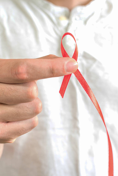 Ένα κοντινό πλάνο ενός νεαρού άνδρα που κρατάει μια κόκκινη κορδέλα - παγκόσμια ιδέα για την ημέρα του AIDS - Φωτογραφία, εικόνα