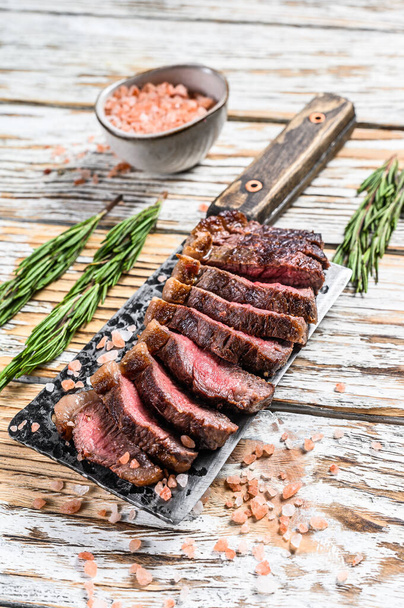 Grilled top sirloin cap or picanha steak on a meat cleaver with herbs. White wooden background. Top view. - Photo, Image