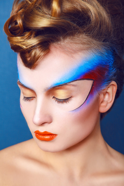 Mujer con maquillaje creativo y peinado sobre fondo azul
 - Foto, Imagen
