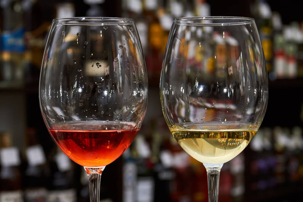 Copo de vinho branco e tinto no fundo de estantes com garrafas de vinho - Foto, Imagem