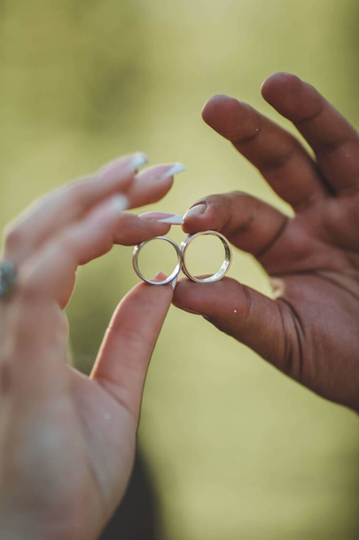 A vertical selective focus shot of bride and groom hand holding wedding rings - Fotó, kép