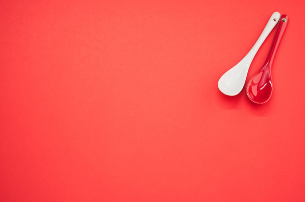 A top view of two small ceramic spoons, one red and one white, placed on a red surface - Foto, afbeelding