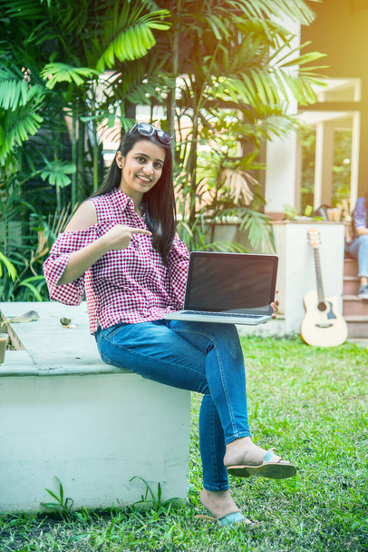 Azji indyjski student w centrum uwagi pracy na laptopie lub czytania książki, podczas gdy inni koledzy w tle, zdjęcie na świeżym powietrzu w kampusie uniwersyteckim - Zdjęcie, obraz