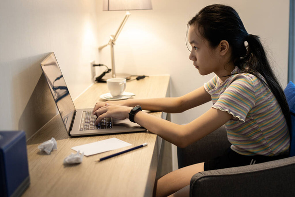 Koncentrált ázsiai diák dolgozik az asztalnál, használja laptop számítógép dolgozni otthonról, szorgalmas tizenéves lány keres extra jövedelem munkát online, szabadúszó, extra pénzt keresni, miután visszatért az iskolából - Fotó, kép