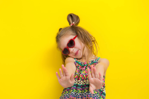 Stüdyonun sarı arka planında güneş gözlüklü şirin küçük kız.. - Fotoğraf, Görsel