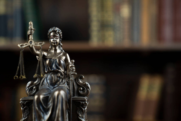 Recht und Gerechtigkeit. Richterkammer. Themis Skulptur auf braunem Schreibtisch. Sammlung juristischer Bücher im Bücherregal. - Foto, Bild