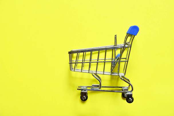 pequeño carrito de compras sobre ruedas sobre fondo amarillo, concepto de compras, descuentos en centros comerciales. espacio de copia. - Foto, Imagen