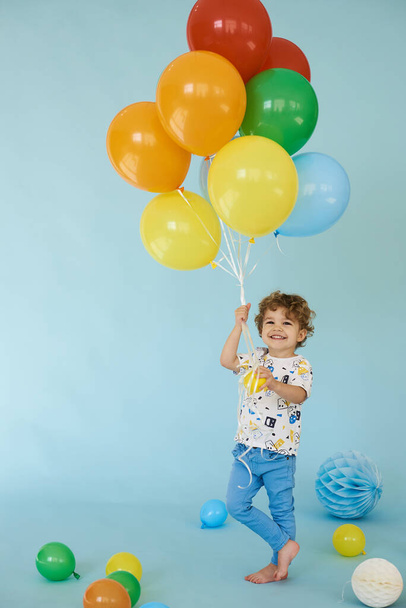 Full length portrait of cheerful boy holding balons posing against blue background - Foto, imagen