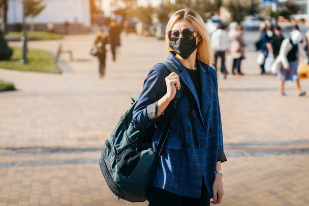 Junge hübsche Modefrau mit Rucksack in Gesichtsverschmutzungsmaske, um sich vor dem Coronavirus in der Stadt zu schützen  - Foto, Bild