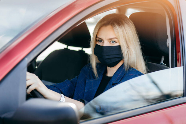 Fiatal lány fekete maszkban ül egy autóban, védő maszk a koronavírus ellen, sofőr egy városi utcán egy koronavírus járvány idején - Fotó, kép