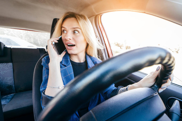 Водій жінка за кермом автомобіля відволікається на телефон і дивиться на сторону
 - Фото, зображення