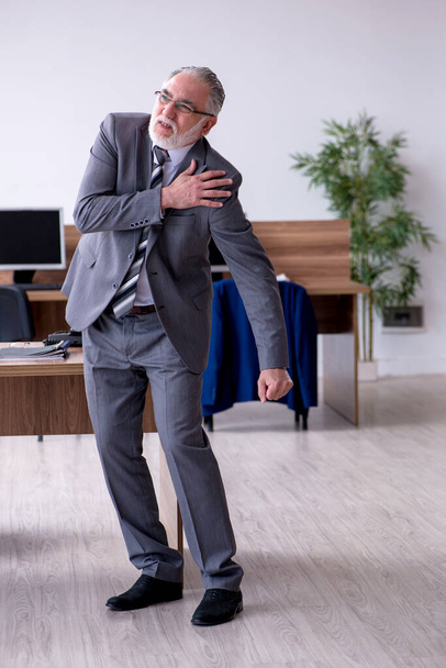Old male employee suffering from radiculitis at workplace - Foto, imagen