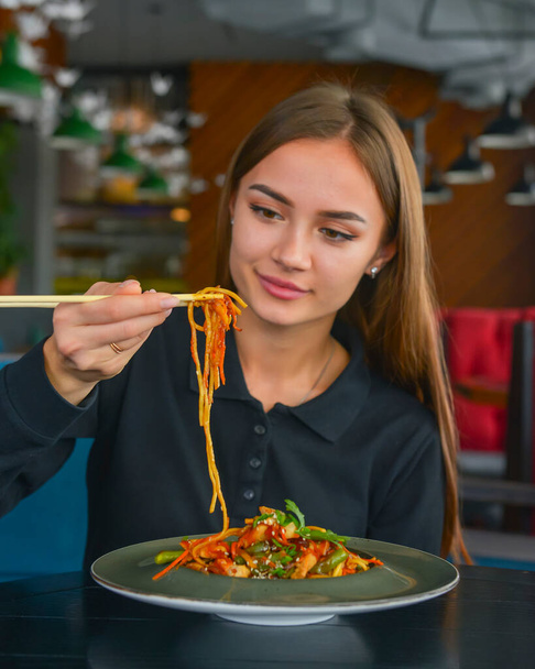 Beautiful young woman eating chinese food called Wok with chopsticks. Wok with meat and fried asparagus in a plate. Still life, eating out in restaurant concept. - Foto, afbeelding
