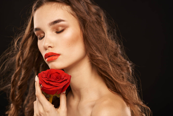 Frau mit roter Rose auf dunklem Hintergrund lange Haare Make-up rote Lippen - Foto, Bild