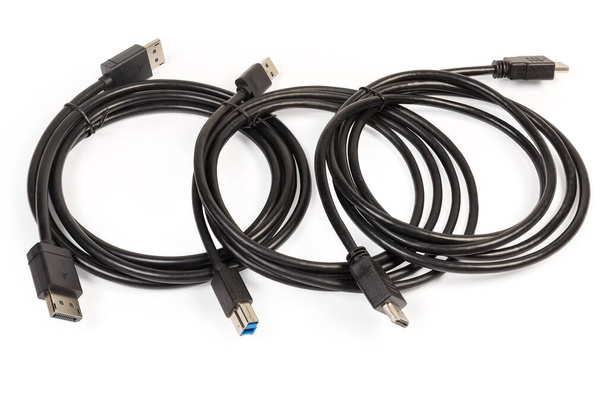 Câbles de différentes interfaces multimédia et informatiques DisplayPort, HDMI et SuperSpeed USB torsadés et attachés en anneaux sur un fond blanc - Photo, image