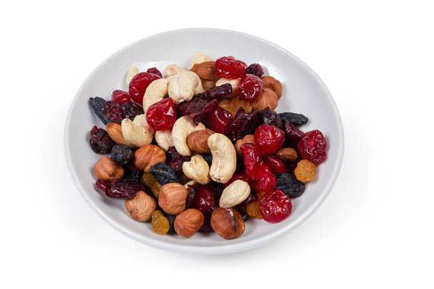 Смесь различных орехов, сухофруктов и ягод на белом блюдце на белом фоне - Фото, изображение