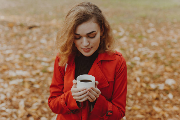 Woman sniff aroma of coffee at the fall day in park - Photo, Image