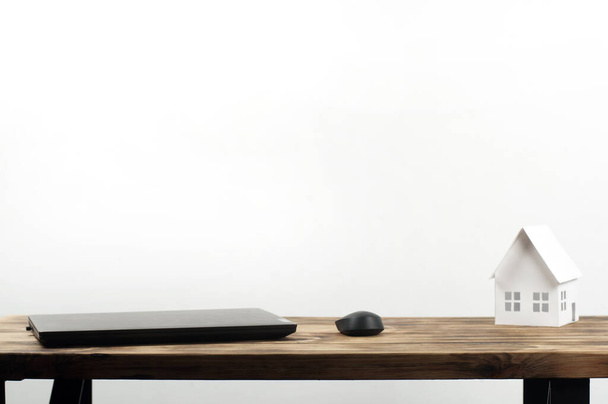 Laptop and computer mouse. Miniature paper house. On a wooden table. - Foto, Imagem