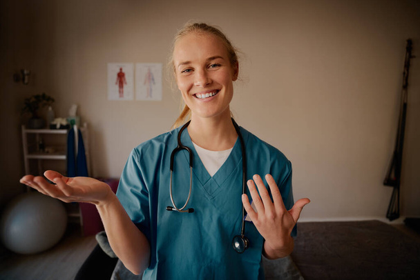 Portrait of happy nurse explaining with hand gestures in medical uniform and stethoscope - Foto, afbeelding