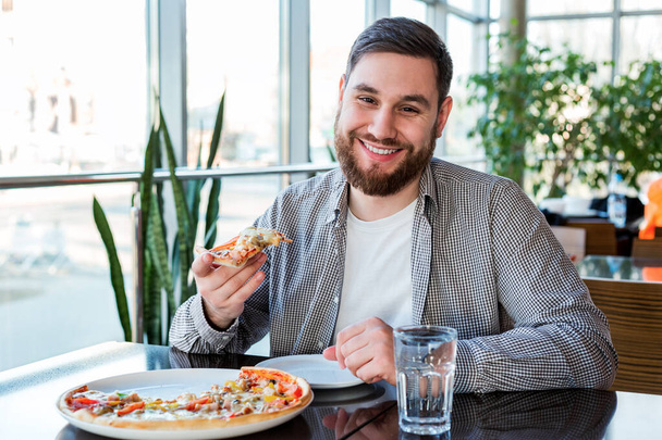 Портрет Счастливый улыбающийся кавказский мужчина, поедающий итальянскую пиццу в пиццерии, сохраняет социальную дистанцию. Вкусная пицца в кафе - Фото, изображение