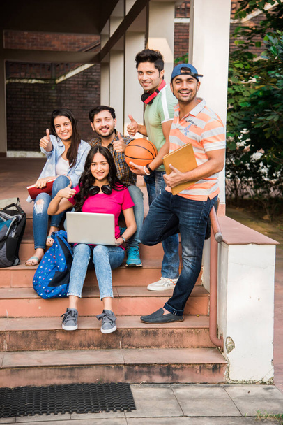 Веселая индийская молодежная группа студентов и друзей колледжа смеется вместе, сидя, стоя или гуляя по кампусу - Фото, изображение