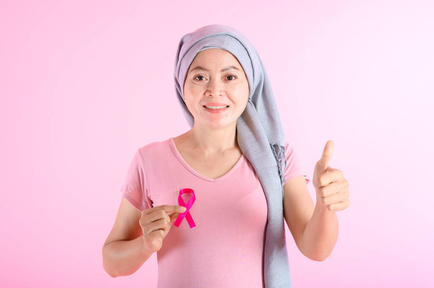 Muzułmanka nosząca hidżab ze wstążką na piersi pokazuje profilaktykę raka piersi. Na różowym tle, koncepcja raka piersi, koncepcja zapobiegania rakowi. - Zdjęcie, obraz