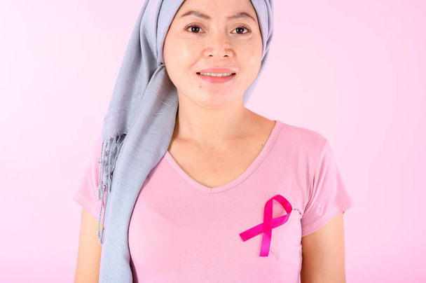 Muzułmanka nosząca hidżab ze wstążką na piersi pokazuje profilaktykę raka piersi. Na różowym tle, koncepcja raka piersi, koncepcja zapobiegania rakowi. - Zdjęcie, obraz