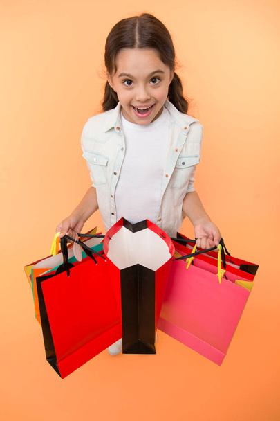 Check out her profitable purchases. Girl carries shopping bags yellow background. Girl fond of shopping. Child cute shopaholic with bunch shopping bags black friday total sale. Exciting shopping - Fotoğraf, Görsel