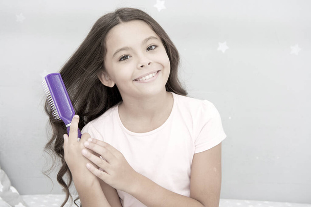 Conditioner or mask organic oil comb hair. Beauty salon tips. Girl long curly hair grey interior background. Child curly hairstyle hold hairbrush or comb. Apply oil before combing hair. Healthy hair - Foto, immagini